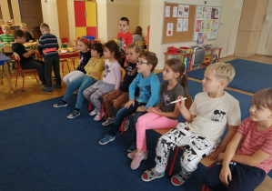 Dzieci siedzą na krzesełkach naprzeciwko tablicy i obserwują zadania